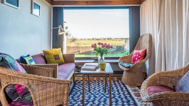 A cozy room with wicker furniture, a view of a field, and a large window with curtains. - The Hut, Walberswick (Walberswick)