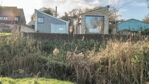 A modern house with a large glass window and a stone wall in front. - The Hut, Walberswick (Walberswick)