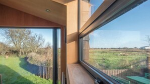 A room with a large window offering a view of a grassy field and trees. - The Hut, Walberswick (Walberswick)
