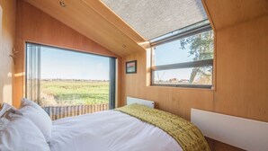 A bedroom with a large bed, a view of a field, and a window with a view of a building. - The Hut, Walberswick (Walberswick)