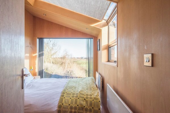 A bedroom with a bed, a window, and a door leading to an outdoor area. - The Hut, Walberswick (Walberswick)