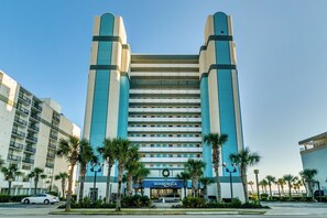 A modern hotel with a prominent 'Boardwalk' sign, featuring a central atrium with a glass facade, surrounded by palm trees and a parking area. - Newly Renovated Oceanfront Corner unit,2 Balconies (Myrtle Beach)