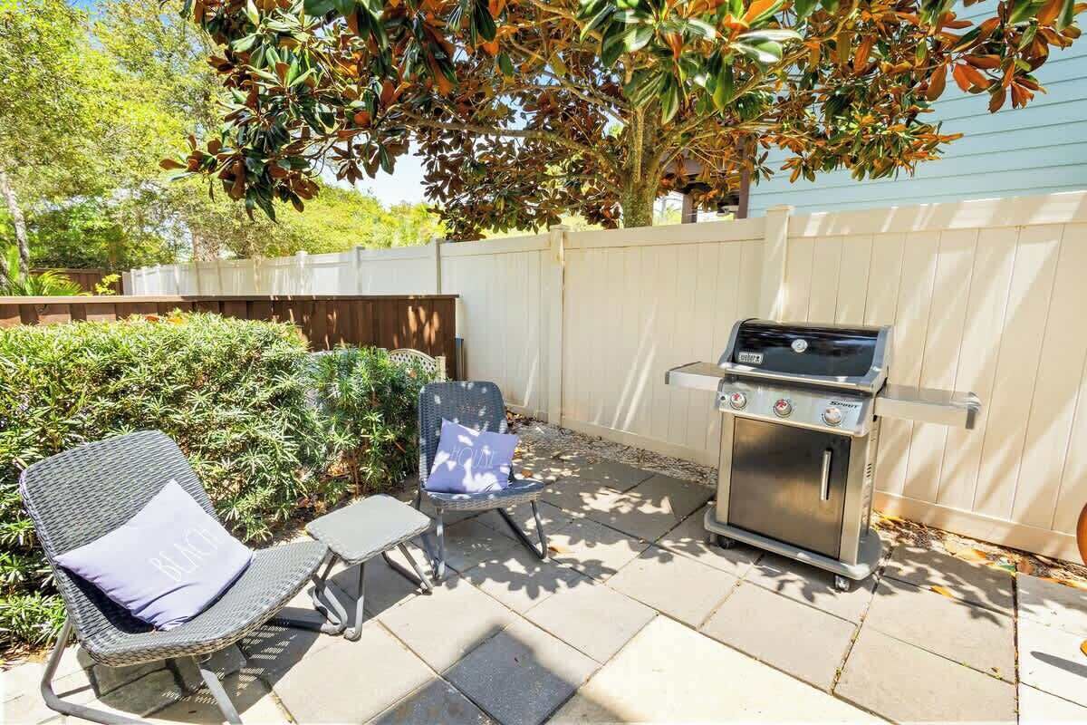 Un jardin avec un barbecue, deux chaises et une petite table.