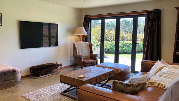 A living room with a brown leather sofa, a wooden coffee table, a brown armchair, and a large window with curtains.