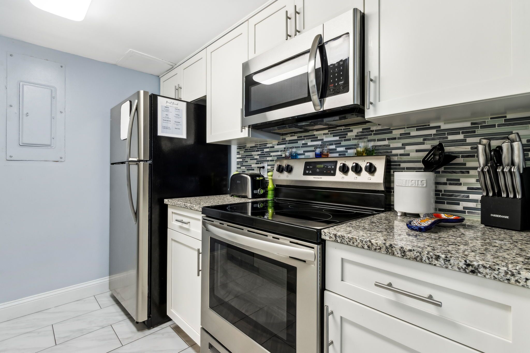 A modern kitchen with stainless steel appliances, a granite countertop, and white cabinetry.
