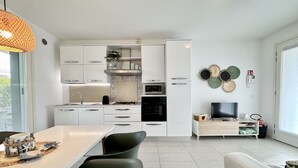 A modern kitchen with white cabinets, a built-in microwave, and a TV on a wooden stand. - Appartamento Forte 3 - Carraro Immobiliare (Lido di Jesolo)