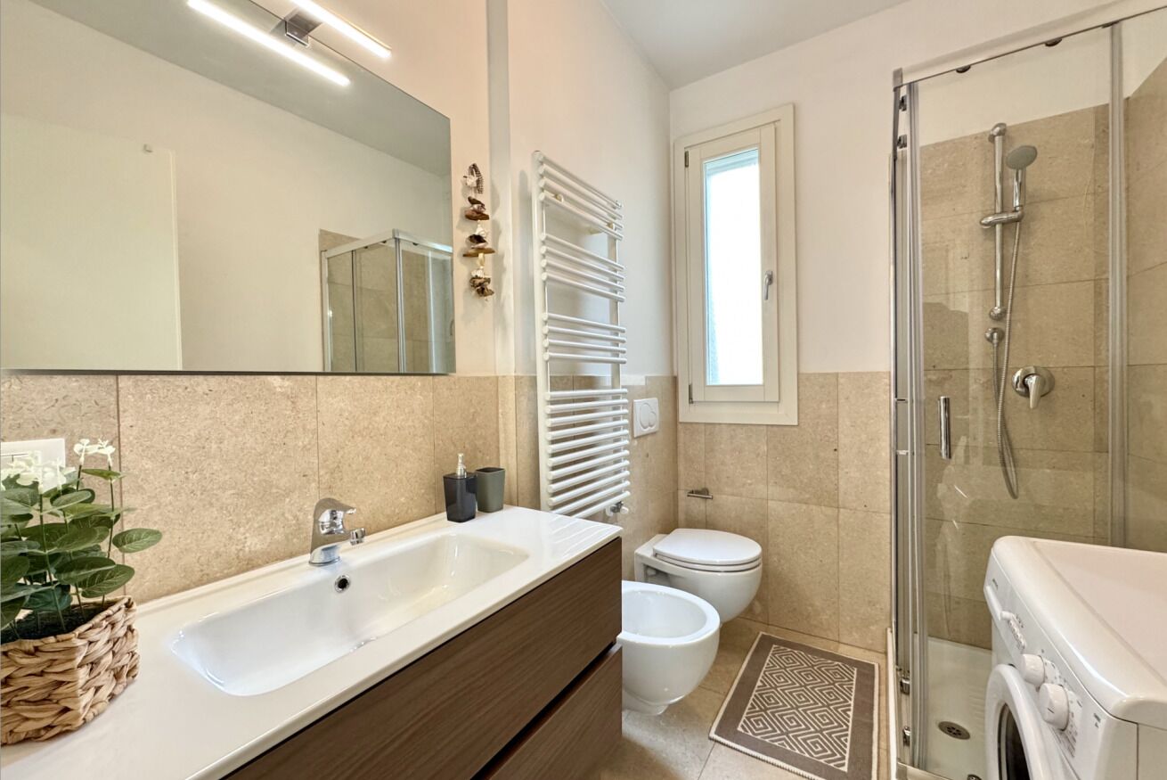 Een moderne badkamer met een grote spiegel, een witte wastafel, een toilet, een douche en een klein raam.