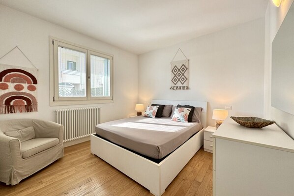 A bedroom with a bed, bedside tables, a chair, a window, and a radiator.