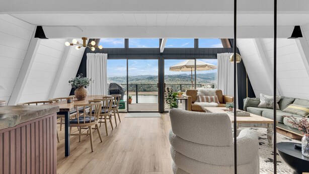 A spacious loft apartment with a high ceiling, a dining area, a cozy seating area, and large windows offering a view of the countryside.