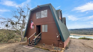 A brown house with a steep roof, a porch, and a flag.