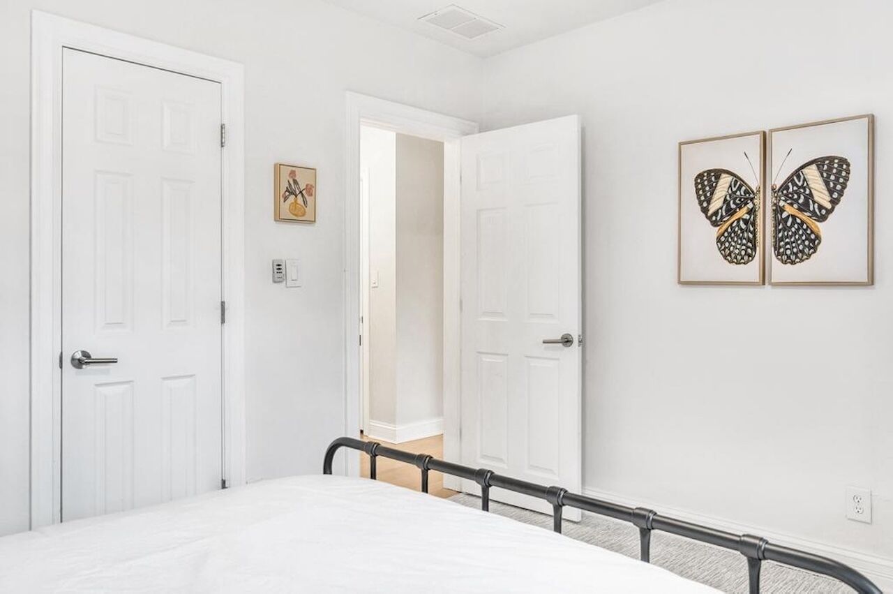 Quarto com cama, paredes brancas, duas portas e arte com borboletas.