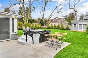 Un jardin avec un jacuzzi, un espace salon couvert et une pelouse bien entretenue.