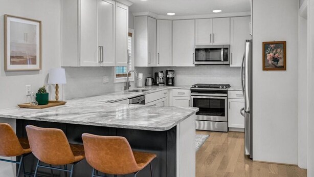 Una cocina moderna con armarios blancos, una isla de mármol y electrodomésticos de acero inoxidable.