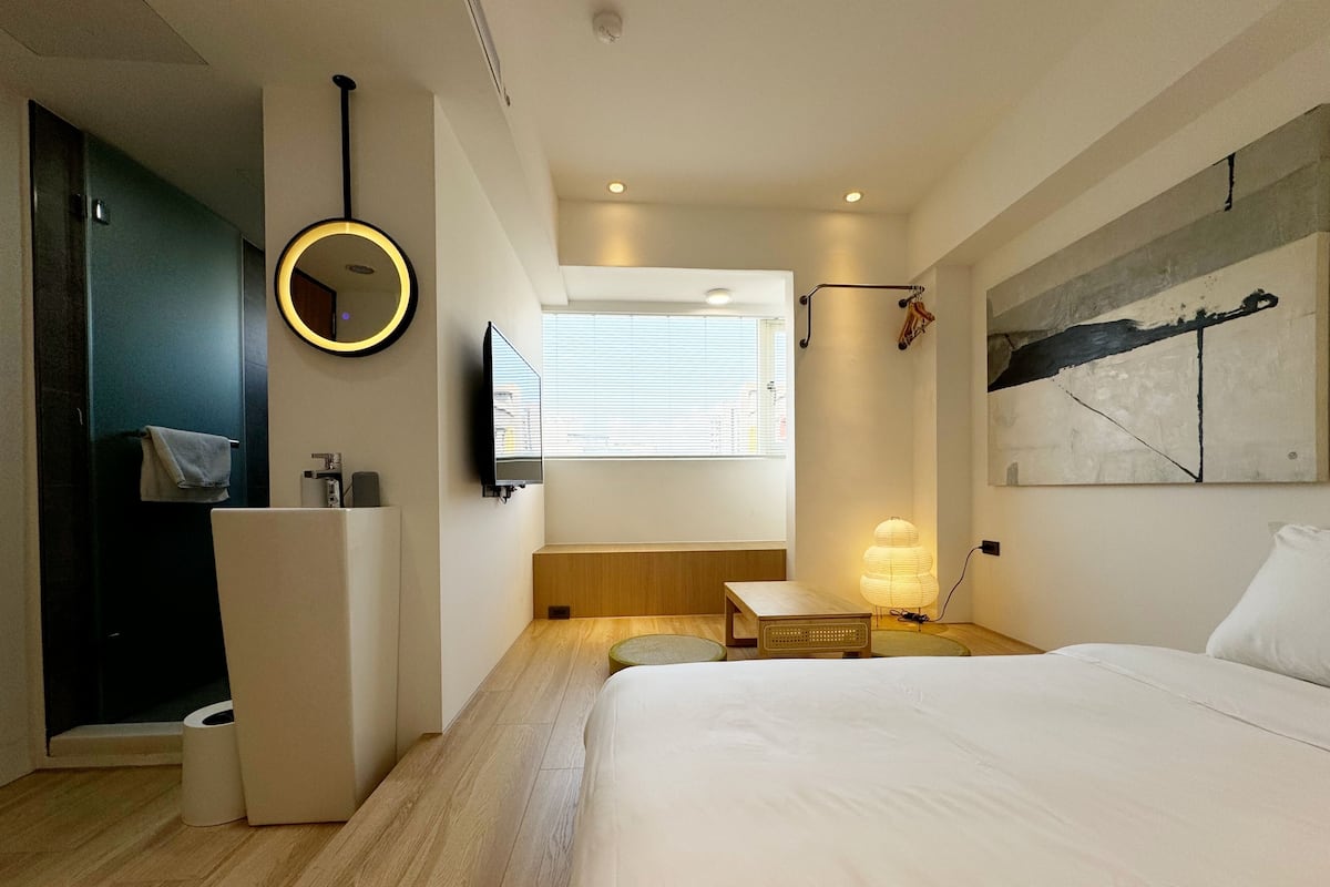 A modern hotel room with a large bed, a flat-screen TV, a wooden bench, and a wall-mounted artwork.