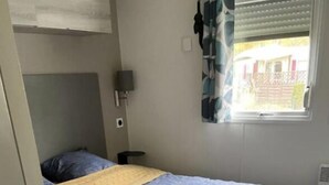 Un dormitorio con cama, mesita de noche, lámpara y ventana con persianas.