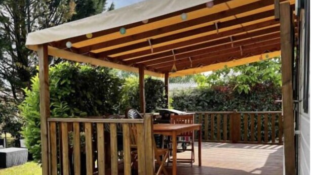 Una terraza de madera con una pérgola, mobiliario exterior y una escalera que lleva a una zona cubierta.