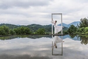 Una persona bailando frente a una superficie reflectante con un paisaje montañoso al fondo.