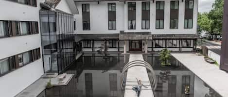 A courtyard with a reflective water feature, modern and traditional architecture, and a person walking.