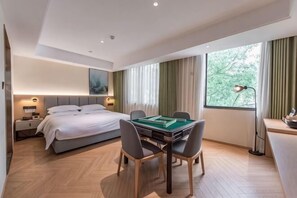 A hotel room with a bed, a desk with a lamp, a dining table with chairs, and a large window with curtains. - Nanxi River Lion Crag Hotel (Yongjia)