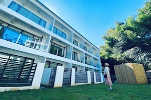 Un edificio moderno de varios pisos con balcones, un patio con césped y una valla de madera.