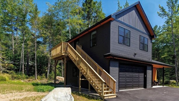 Une cabane à deux étages, avec un escalier en bois menant à un porche abrité, le tout entouré d’une forêt.