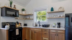 Une cuisine avec des meubles en bois, un poêle noir, un four à micro-ondes, un évier et une fenêtre donnant sur les arbres.