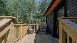 Une terrasse en bois avec deux fauteuils en osier et une petite table, entourée de grands arbres.