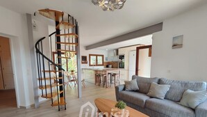 A modern living room with a grey sofa, wooden coffee table, and a spiral staircase leading to an upper floor. - Los Palmitos, Calonge - Costa Brava (Calonge)