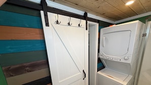 A laundry room with a white washing machine and dryer, a door with hooks, and a wooden ceiling.
