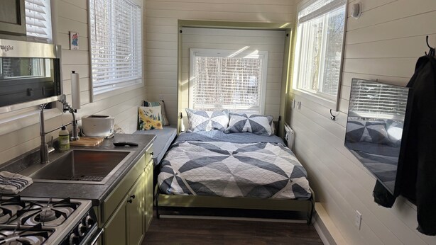 A compact, well-lit room with a bed, a small kitchenette, and a window providing natural light.