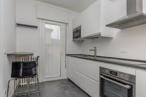 Une cuisine de taille réduite avec des meubles blancs, un four en acier inoxydable, un four à micro-ondes et une chaise noire.