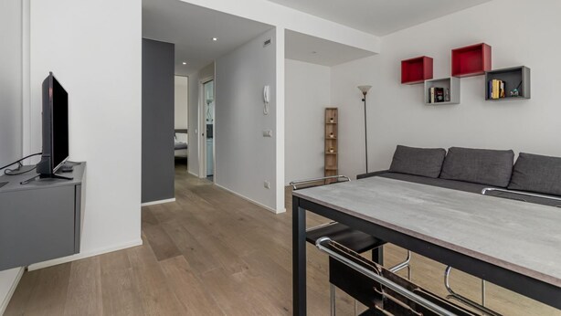 A modern living room with a dining table, a TV on a cabinet, and a hallway leading to another room. - GuestHost - Charming Apartment in Venice Mestre (Venezia)