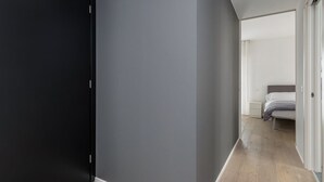 A hallway with a black door, grey walls, and a bed with white bedding in the adjacent room. - GuestHost - Charming Apartment in Venice Mestre (Venezia)