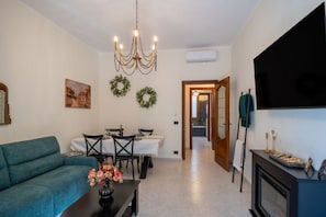 Una sala de estar con sofá, mesa de comedor, candelabro y televisor de pantalla plana.