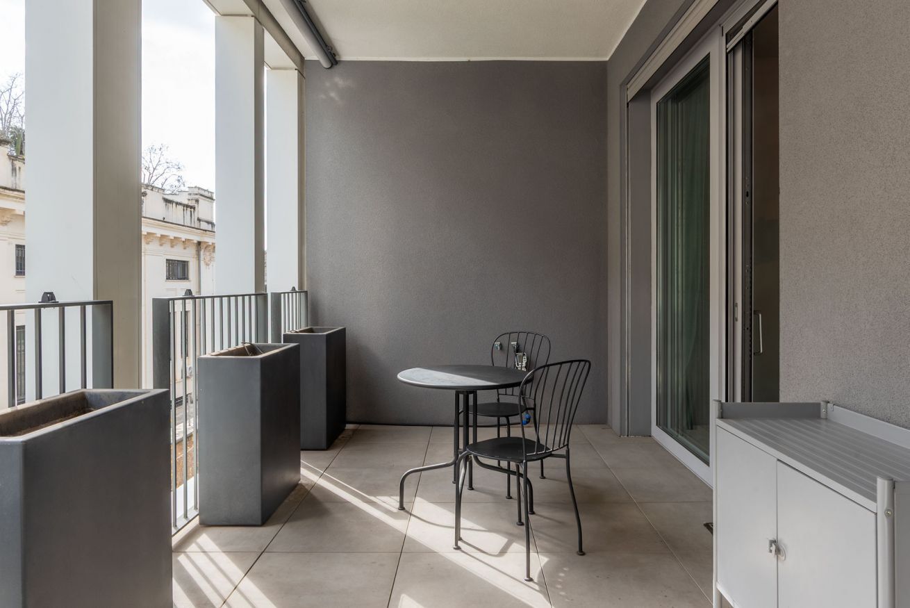 Een balkon met een tafel, stoelen, een afvalbak en een raam.