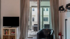 Un salon moderne doté d’un téléviseur à écran plat, d’un fauteuil en cuir, d’un canapé rouge, d’une bibliothèque et offrant une vue sur le balcon extérieur.