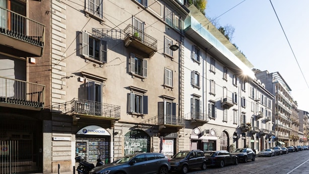Une rangée d’immeubles à étages avec des balcons, un restaurant de sushis et des voitures garées le long d’une rue pavée.