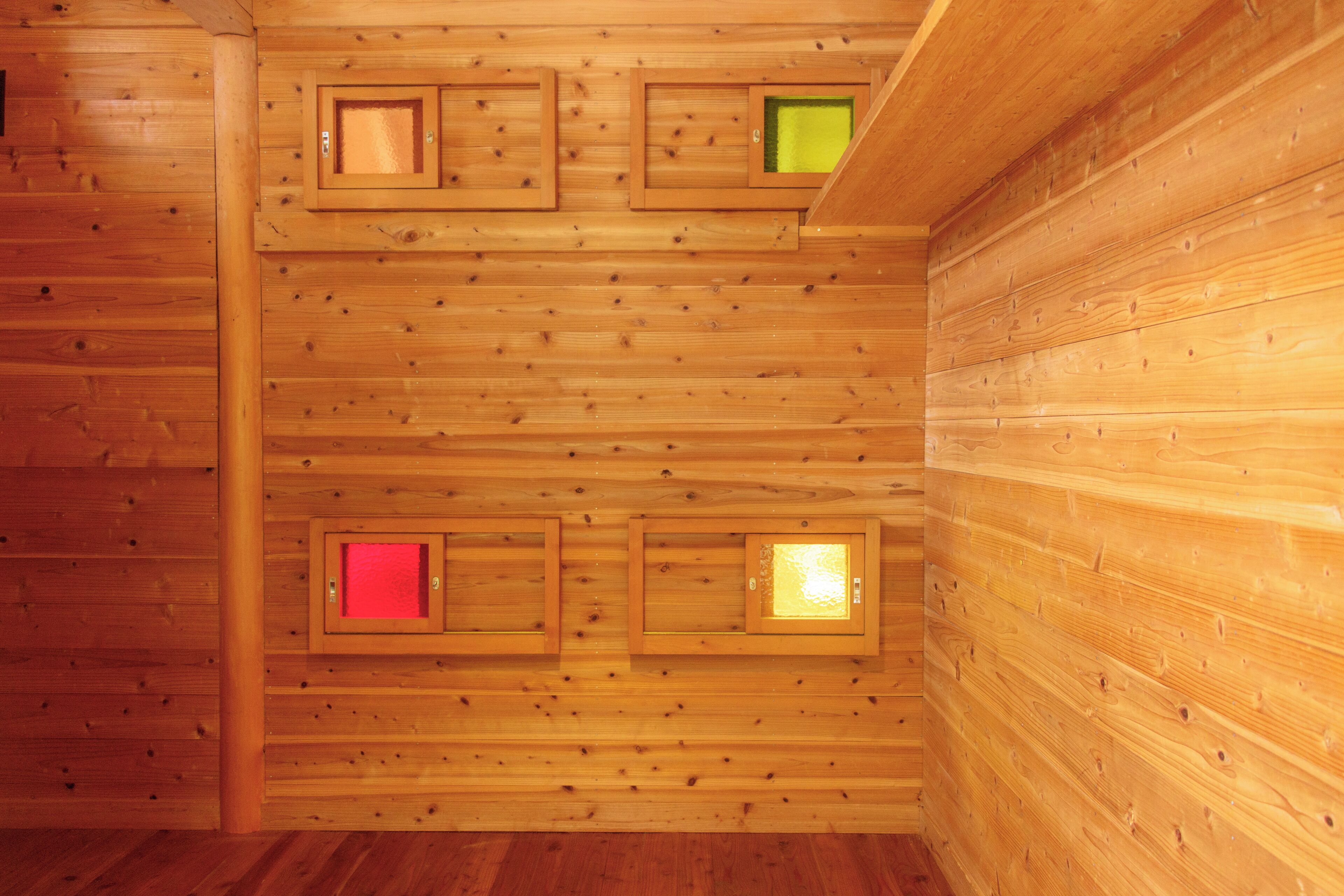 A wooden cabin interior with a sloped ceiling and three small windows.