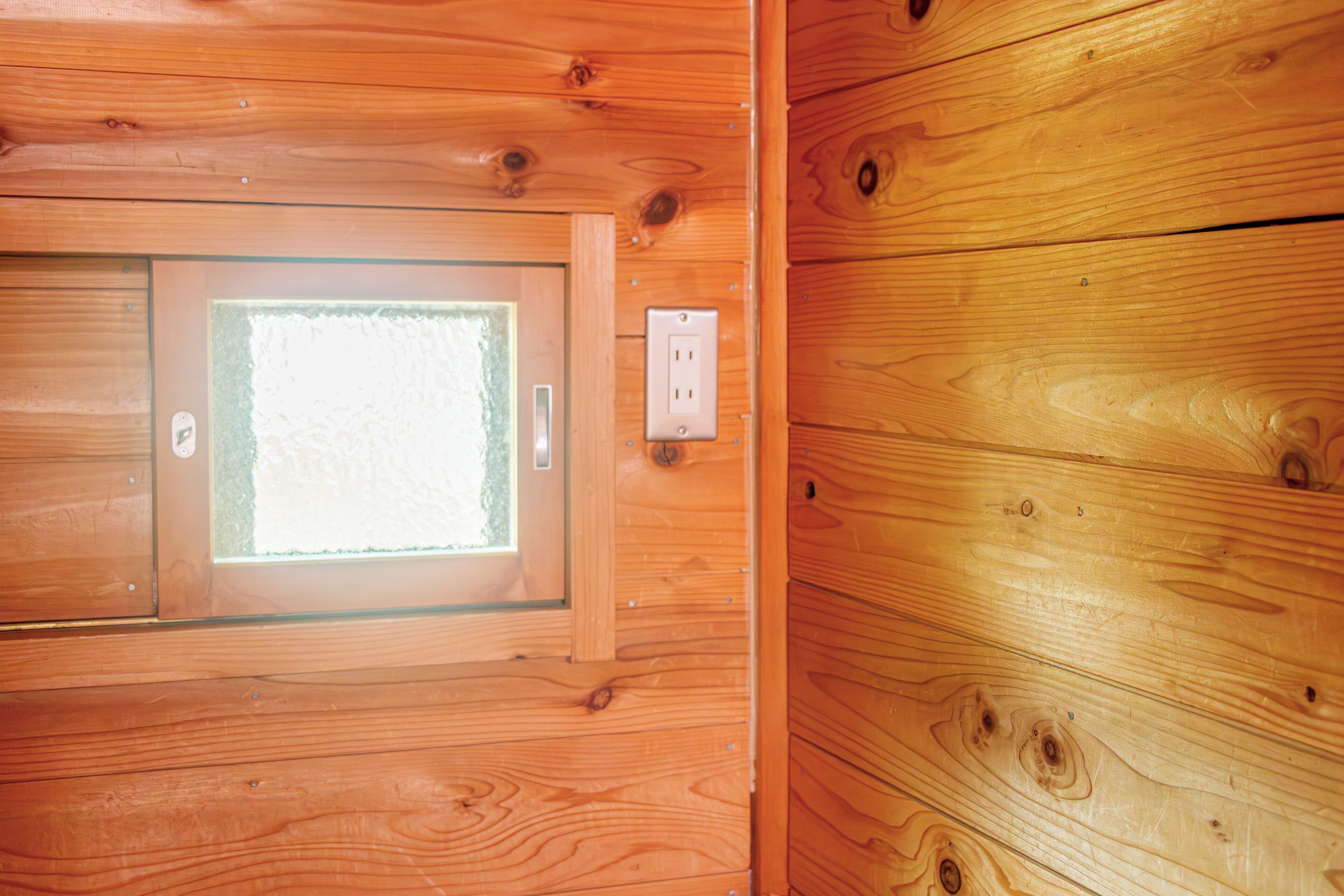A wooden cabin interior with a window, a door, and an electrical outlet.