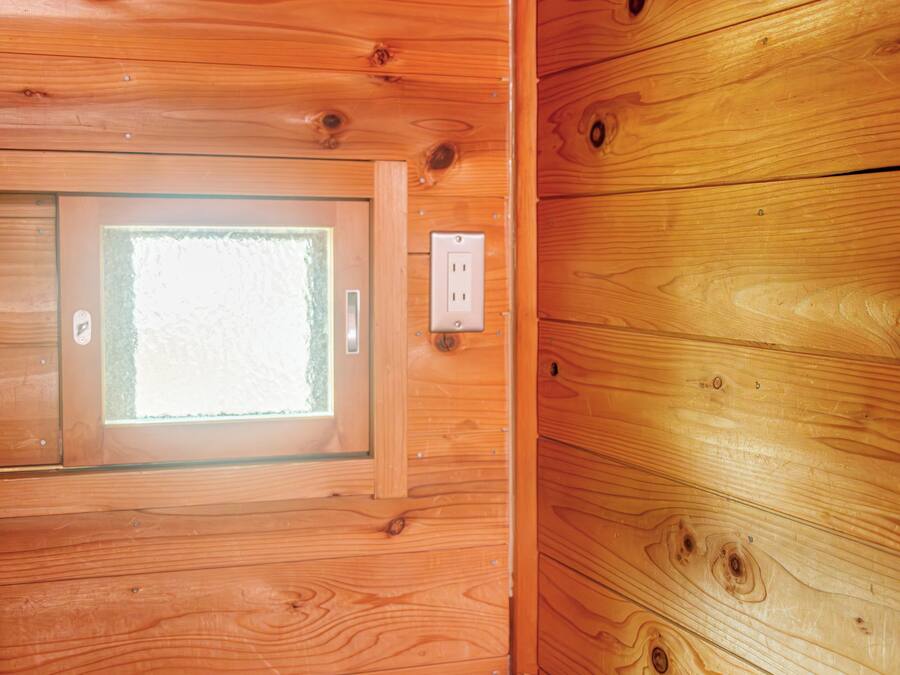 A wooden cabin interior with a window, a door, and an electrical outlet.