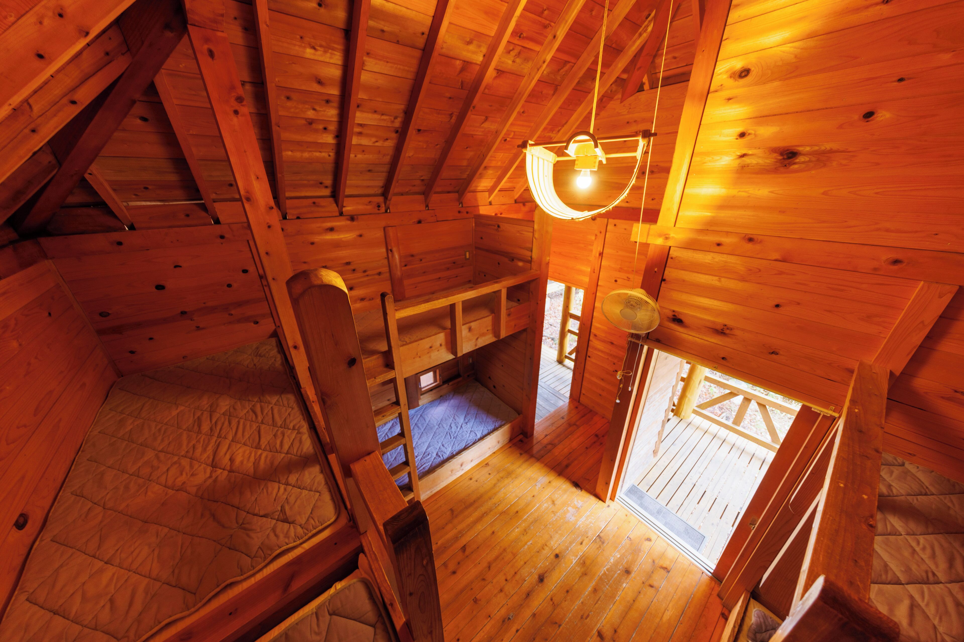 A wooden cabin with a loft bed, a small seating area, and a window.