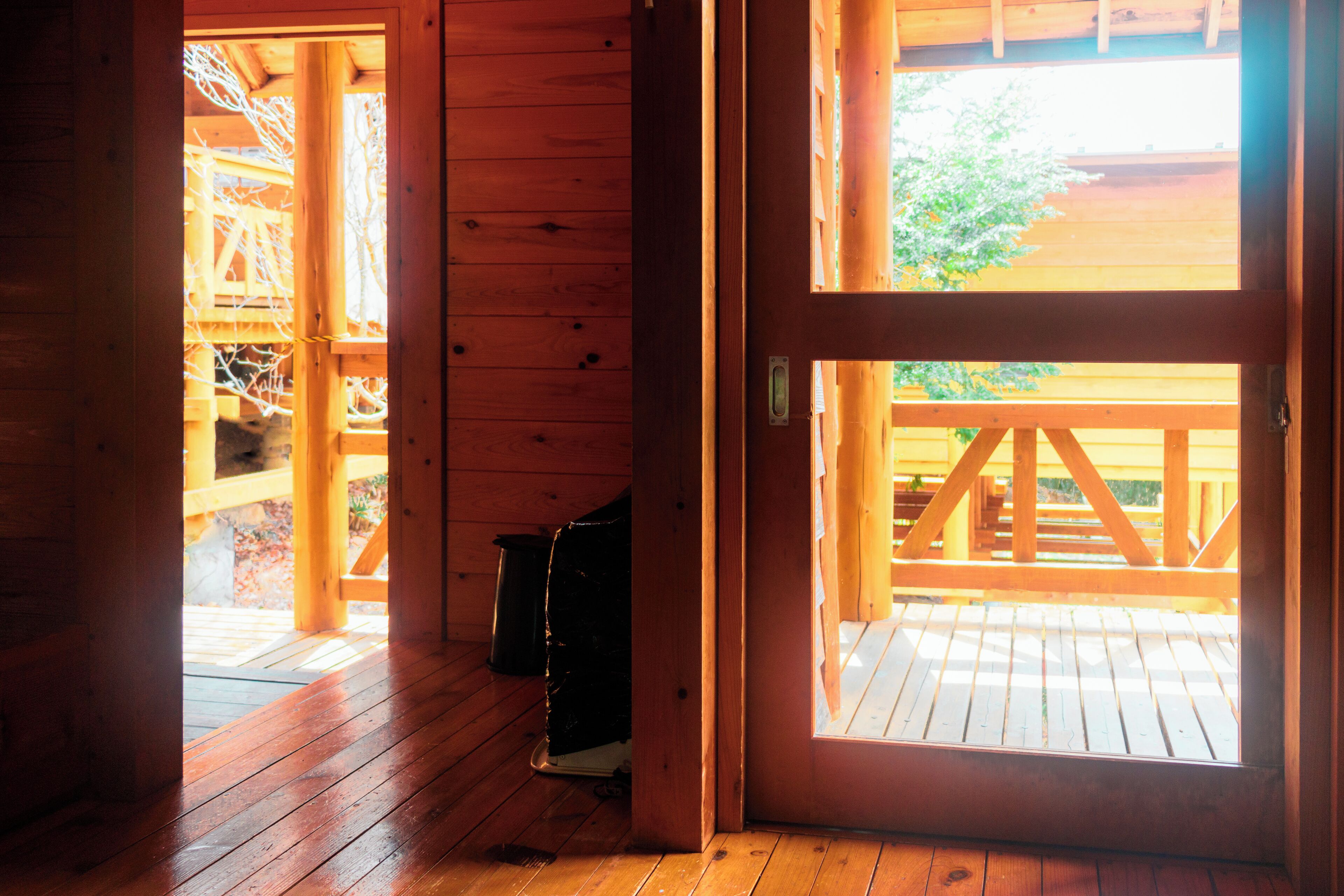 A wooden cabin interior with a wooden door leading to an outdoor deck.