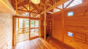Interior de una cabaña de madera con terraza, ventanas amplias y techo inclinado.