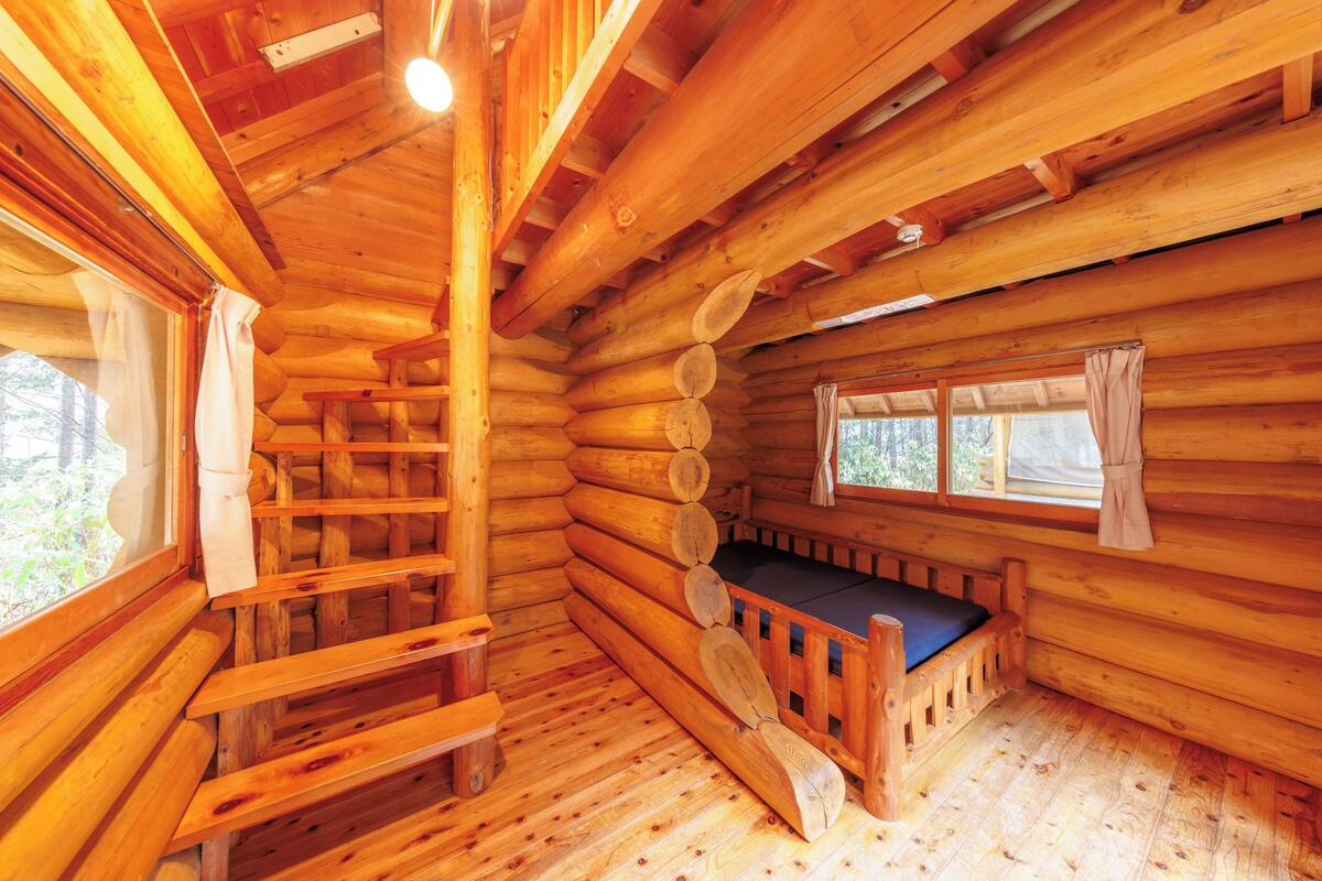 Interior d'una cabana de fusta amb una banca de fusta, una escala i una finestra amb cortines.