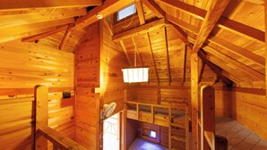 Una cabaña de madera con habitación tipo loft, una ventana pequeña y techo de madera.
