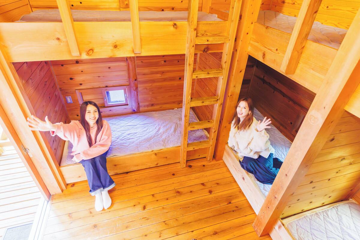 Habitació amb lliteres de fusta, una escala i una finestra petita.