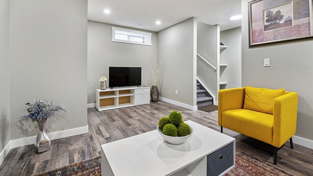 A modern living room with a white coffee table, a yellow sofa, a flat-screen TV, and a staircase.