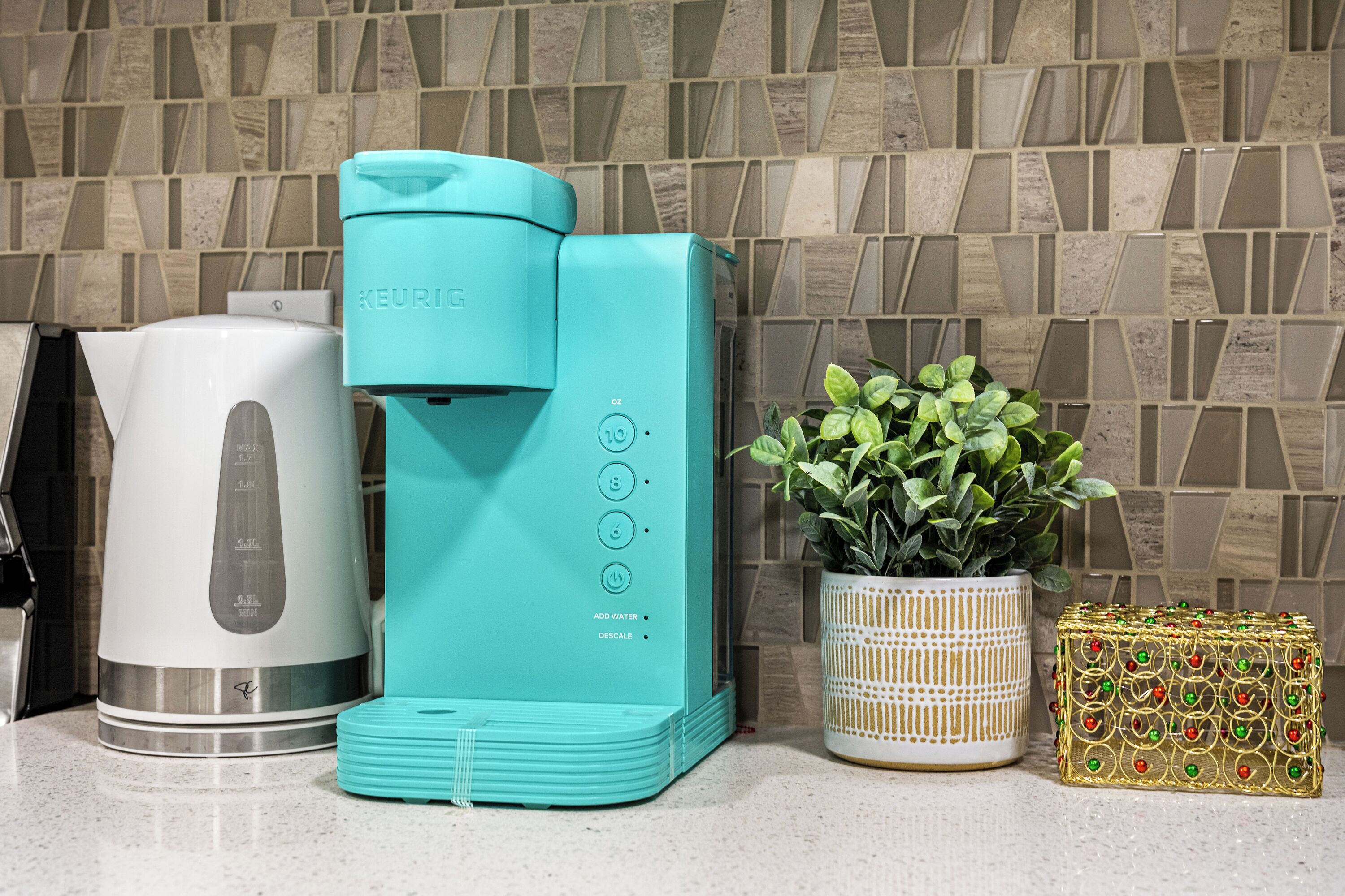 A kitchen with a coffee maker, a kettle, and a potted plant.