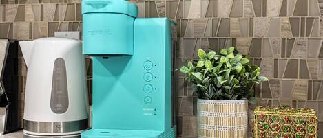 A kitchen with a coffee maker, a kettle, and a potted plant.