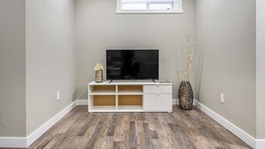 A room with a flat-screen TV on a white entertainment unit, a small window, and a decorative vase with branches.